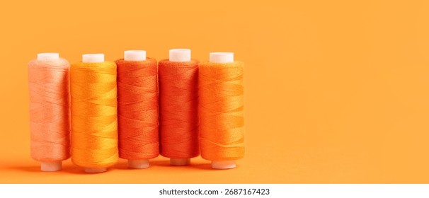 Spools of threads on orange background with space for text