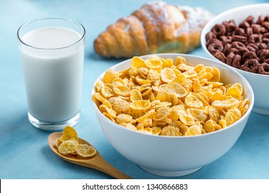 Spoon And Bowl With Chocolate Rings, Yellow Frosted Corn Flakes, Croissant And A Glass Of Milk For Dry, Cereals Breakfast 