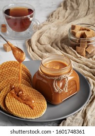 A Spoon With Carmel Sauce Pours Wafers On A Plate. Close-up. Jar Of Homemade Caramel Sauce. Selective Focus, Vertical Orientation