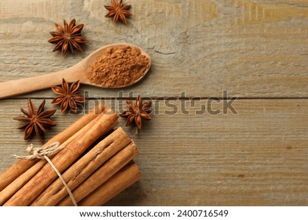 Spoon with cinnamon powder, sticks and star anise on wooden table, flat lay. Space for text