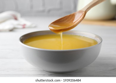 Spoon of clarified butter over bowl on white wooden table