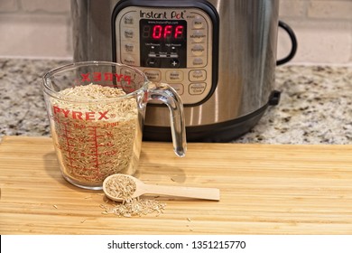 A spoon and a Cup of Brown Rice on a wood cutting board and an Instant Pot in the background