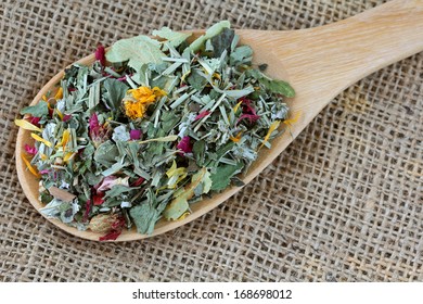 A Spoon Of Dried Herbal Tea With Flowers On A Hemp Fabric Background. It Consists Of Lemon Balm, Rose Petal, Marigold, Cornflower, Blackberry, Lemongrass Leaves With Antioxidant Benefit