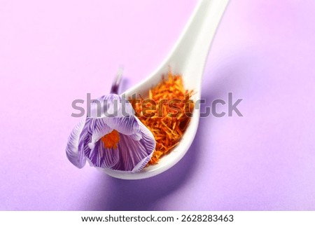 Spoon with dried saffron threads and crocus flower on lilac background