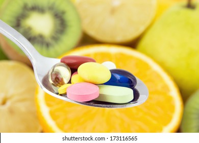 Spoon full of colorful pills against the background of juicy fruits