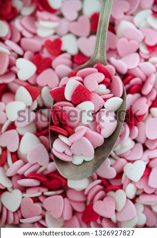 Spoon full of tiny heart-shaped sugar sprinkles in red, pink and white for Valentine's day card, symbol for love or romantic feelings used for baking or cake or cupcake decoration on more hearts