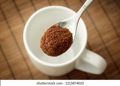 Spoon with ground coffee over the white empty cup against a brown bamboo background. Making coffee - Shutterstock ID 1215874033