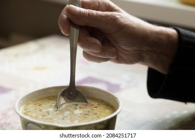 Spoon in the hand of an elderly man with which he eats noodle soup in a cardboard box - Shutterstock ID 2084251717