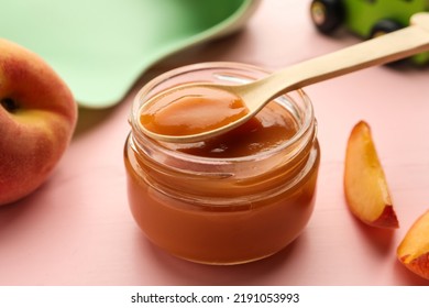 Spoon With Healthy Baby Food Over Glass Jar On Pink Wooden Table, Closeup