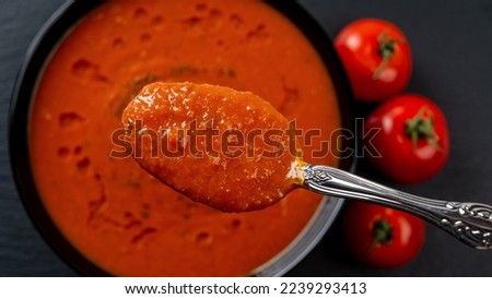 Spoon of hot tomato soup over bowl closeup. Eating vegetable dish of pureed roasted tomatoes, garlic and basil. Healthy vegetarian dish. Mediterranean cuisine. Focus on spoon. Top view.