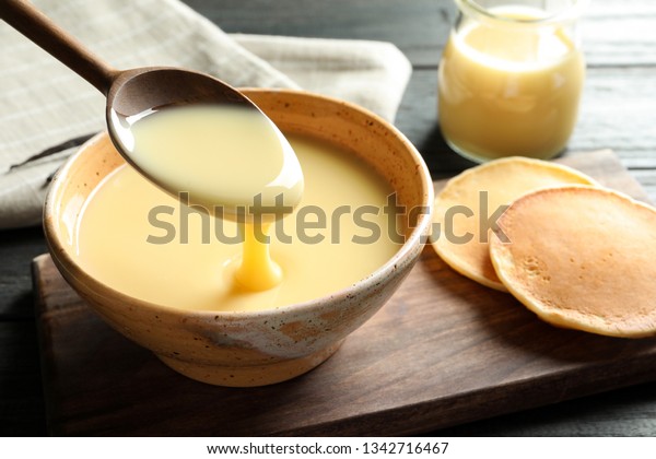 Spoon of pouring condensed milk over bowl on\
table, space for text. Dairy\
products