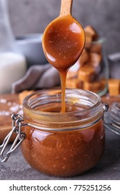 Spoon With Tasty Caramel Sauce Over Jar On Table