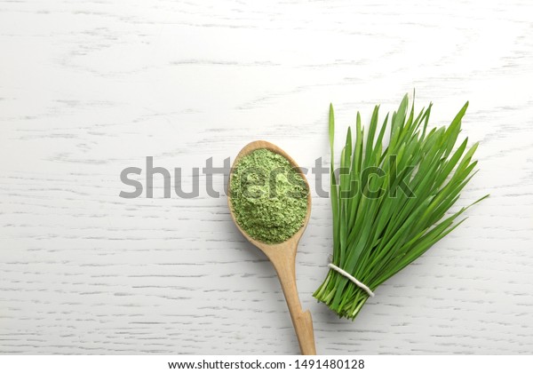 Spoon of wheat grass powder and green\
sprouts on white wooden table, flat lay. Space for\
text