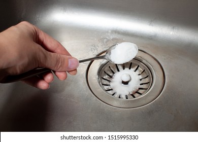 A spoonful of baking soda in his hand pours onto the dirty dishwasher in the kitchen. Using soda to clean the sink.