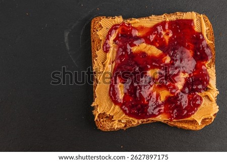 A spoonful of creamy peanut butter is generously layered on a toasted slice of bread, topped with rich grape jelly. The colors contrast beautifully against the dark background.
