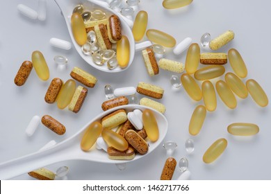 Spoons with a handful of nutraceuticals. There's a lot of pills nearby. White background.