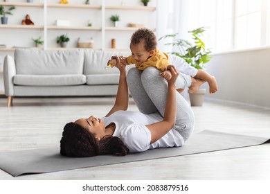 Sport Activities With Baby. Young Black Mom Exercising With Her Infant Son At Home, Happy African American Woman Balancing Baby On Knees While Training On Fitness Mat In Living Room, Copy Space - Powered by Shutterstock