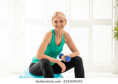 Sport Activities For Older People. Smiling Mature Woman Exercising With Fitball And Dumbbell, Beautiful Elderly Lady Training At Home, Sitting On Swiss Ball And Looking At Camera, Copy Space - Powered by Shutterstock