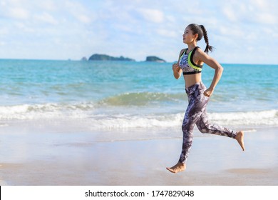 Sport Aisan Woman Running Barefoot On Beach . Fitness Runner Female Wearing Sportswear Jogging On Sea Background Outdoor. Fit Beautiful Girl Workout Training Cardio In Summer