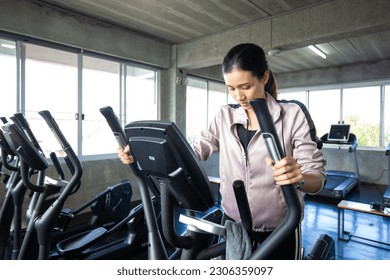 Sport asian woman working out on elliptical machine in fitness room cardio exercise - Powered by Shutterstock