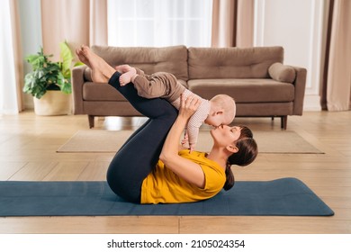 Sport with baby. Fit mom kissing her toddler son while holding him on her legs and doing postpartum recovery exercise on fitness mat at home.Sporty woman exercising together with her little baby