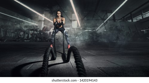 Sport. Battle ropes session. Attractive young fit sportswoman working out in functional training gym doing exercise with battle ropes.