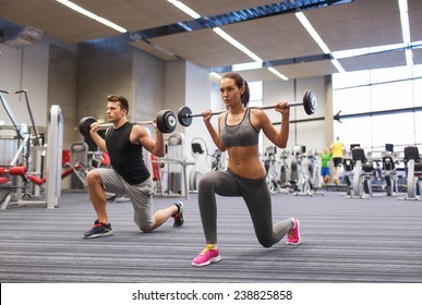 Sport, Bodybuilding, Lifestyle And People Concept - Young Man And Woman With Barbell Flexing Muscles And Making Shoulder Press Lunge In Gym