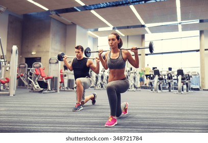 Sport, Bodybuilding, Lifestyle And People Concept - Young Man And Woman With Barbell Flexing Muscles And Making Shoulder Press Lunge In Gym