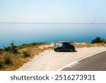 Sport car with a roof box, parked near a sharp turn on a coastal cliff road, with the azure sea below