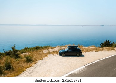 Sport car with a roof box, parked near a sharp turn on a coastal cliff road, with the azure sea below - Powered by Shutterstock