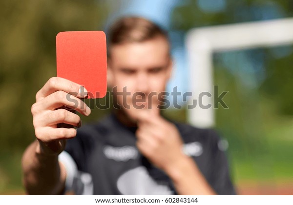 sport, caution, game\
and people - close up of referee hands with whistle showing red\
card on football field