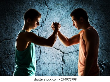 sport, competition, strength and people concept - two young men arm wrestling over concrete wall background