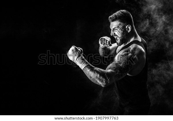 Sport concept. Sportsman muay thai boxer\
fighting on black background with\
smoke.
