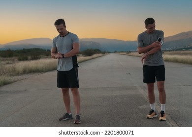 Sport Couple Looking At A Smartwatch While Standing On The Country Road. Resting After Jogging And Running Exercise And Checking Heart Rate And Pulse.