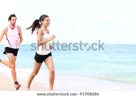 sport - couple running on beach training for marathon run. Young multiracial couple runners, smiling asian female fitness model and caucasian male model.
