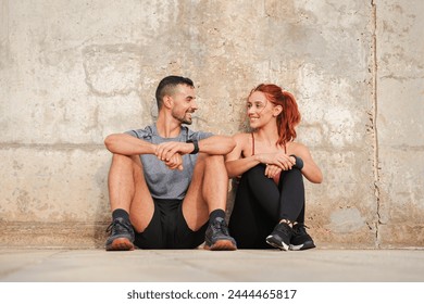 Sport couple taking a break of the workout. Tired young people looking each other, sitting on the floor, recovering energy and having a conversation. Coach man and athletic woman talking and resting - Powered by Shutterstock