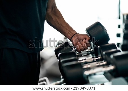 Sport Equipment Concept. Unrecognizable Black Male Athlete Taking Dumbbell From Rack At Gym, Closeup Shot Of African American Man Choosing Barbells, Preparing For Bodybuilding Workout, Cropped