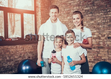 Sport Family In The Fitness Club During A Break. Healthy Lifestyle. Training Exersises. Sunny Day. Resting Together. Work Out. White Shirt. Sunny Day. Active Occupation. Parents And Children.