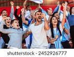 Sport fans cheering at the game on stadium. Wearing blue and white colors to support their team. Celebrating with flags and scarfs.