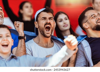 Sport fans cheering at the game on stadium. Wearing blue and white colors to support their team. Celebrating with flags and scarfs. - Powered by Shutterstock