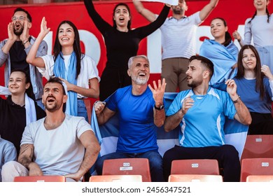 Sport fans cheering at the game on stadium. Wearing blue and white colors to support their team. Celebrating with flags and scarfs. - Powered by Shutterstock