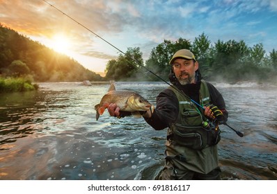 Sport fisherman holding trophy fish. Outdoor fishing in river during sunrise. Hunting and hobby sport.