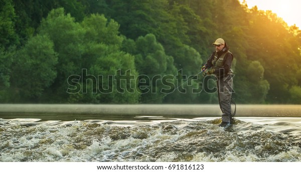Sport fisherman hunting\
predator fish. Outdoor fishing in river during sunrise. Hunting and\
hobby sport.