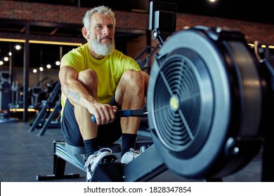 Sport And Fitness After 50. Strong Mature Athletic Man In Sportswear Exercising On Rowing Machine At Gym