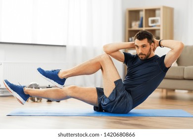 sport, fitness and healthy lifestyle concept - man making bicycle crunch on exercise mat and flexing abs at home