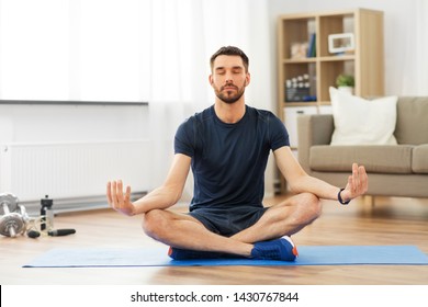 sport, fitness and healthy lifestyle concept - man meditating in lotus pose on yoga mat at home
