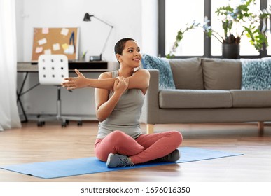 sport, fitness and healthy lifestyle concept - happy smiling young african american woman stretching arm at home