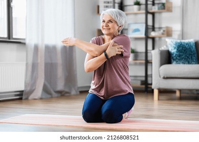 sport, fitness and healthy lifestyle concept - smiling senior woman exercising on mat and stretching arm at home - Powered by Shutterstock