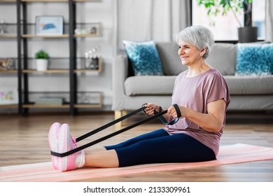 Sport, Fitness And Healthy Lifestyle Concept - Smiling Senior Woman Exercising With Resistance Band On Mat At Home