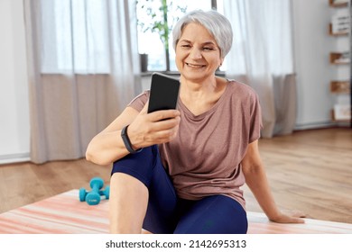 Sport, Fitness And Healthy Lifestyle Concept - Smiling Senior Woman With Smartphone Exercising On Mat At Home